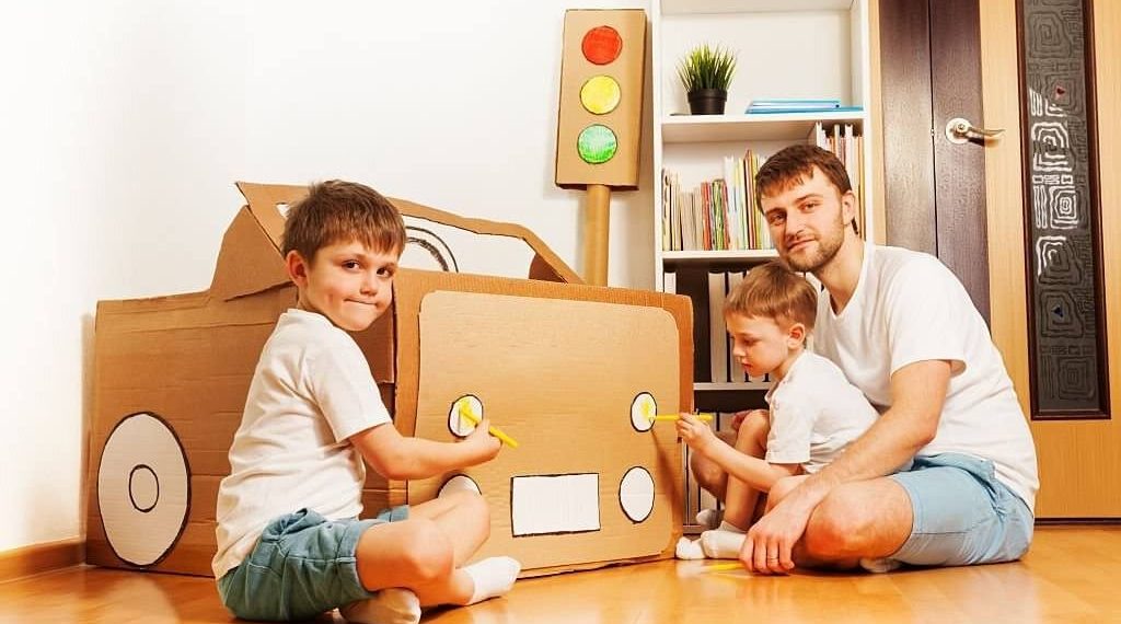 Father and children painting a cardboard house together for their family home project goal