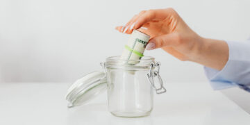 Lady putting a bundle of dollars in to a jar