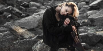Lonely and sad woman setting on rocks in a beach