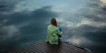 Depressed woman in green jacket sitting at river bank at dusk-ashwagandha and depression