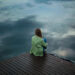 Depressed woman in green jacket sitting at river bank at dusk-ashwagandha and depression