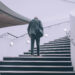 Old man with parkinson's in grey suit hesitantly walking up concrete stairs-ashwagandha and parkinson's