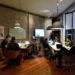 Group of employees sitting at a large table working on computers and discussing-cross team collaboration best practices