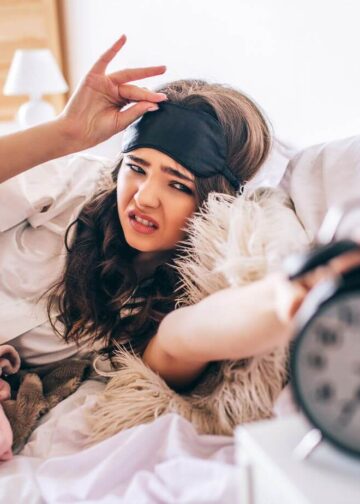 Dark haired beautiful young brunette wake up in her bed and reaching out to the alarm clock-reasons why lazy people are more likely to be successful