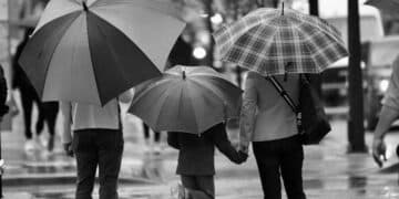 Grayscale photography of three person's holding umbrella