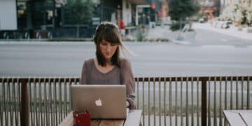Woman in gray shirt sitting on bench in front of macbook
