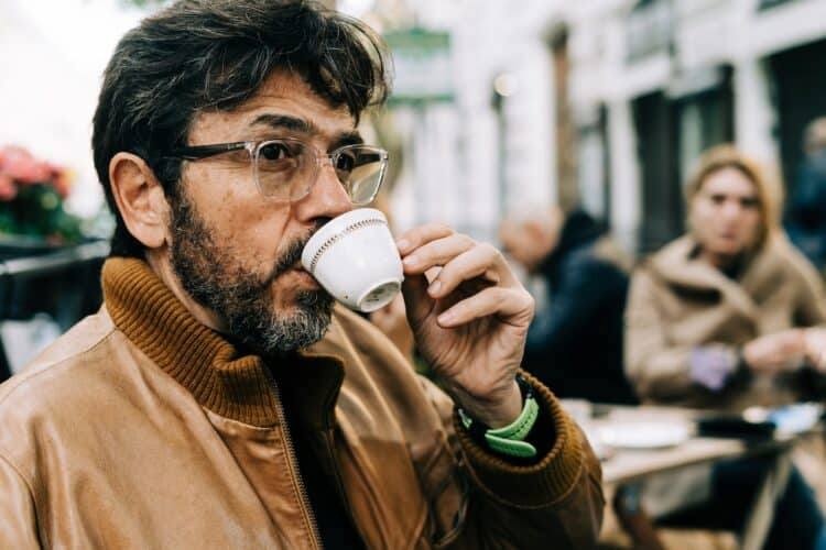 Man in brown jacket drinking on white ceramic mug